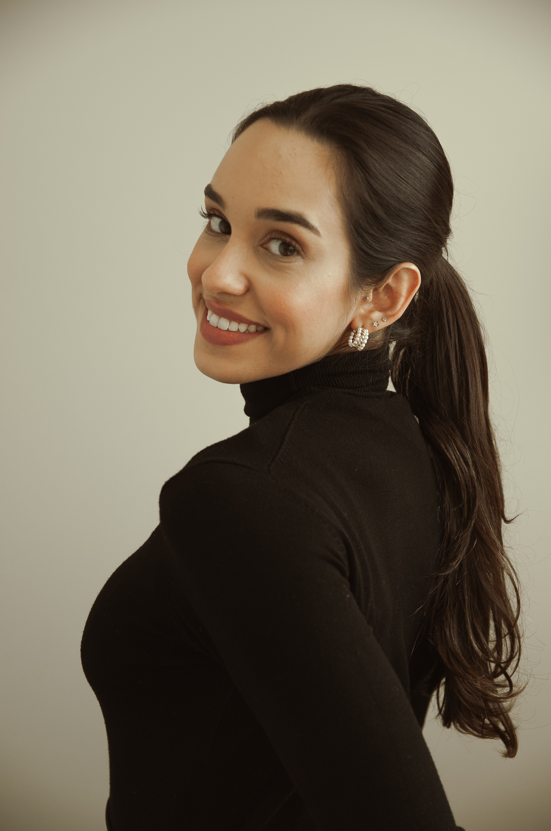 Beatriz Albuquerque, nutricionista, olhando para a câmera por cima do ombro, em retrato de estúdio com fundo neutro