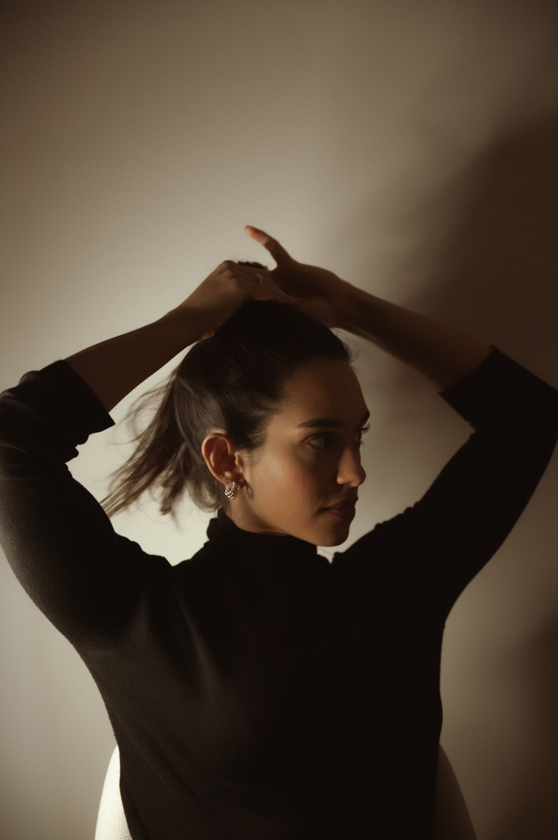 Retrato em contraluz de Bia ajustando o cabelo, em estúdio com luz dramática